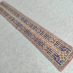 Puede incluir: Una alfombra larga y estrecha con un patrón geométrico en tonos azules, naranjas y beige. La alfombra tiene un borde con flecos.