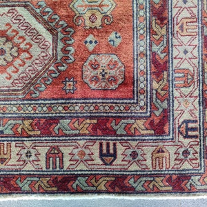 May include: Close-up of a red, beige, and blue patterned rug with intricate designs. The rug has a fringe border and a white backing.