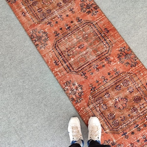 K&ouml;nnte beinhalten: Ein rot-blauer Teppich mit geometrischem Muster. Der Teppich liegt auf einer grauen Oberfl&auml;che.