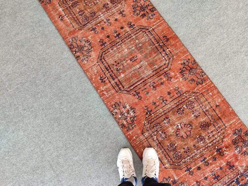 K&ouml;nnte beinhalten: Ein rot-blauer Teppich mit geometrischem Muster. Der Teppich liegt auf einer grauen Oberfl&auml;che.