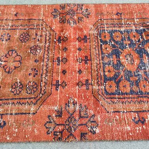K&ouml;nnte beinhalten: Ein Vintage-Teppich mit einem verblassten roten Hintergrund und komplizierten blauen und orangefarbenen Blumenmustern. Der Teppich hat einen abgenutzten Look und ist mit einem traditionellen Design gewebt.