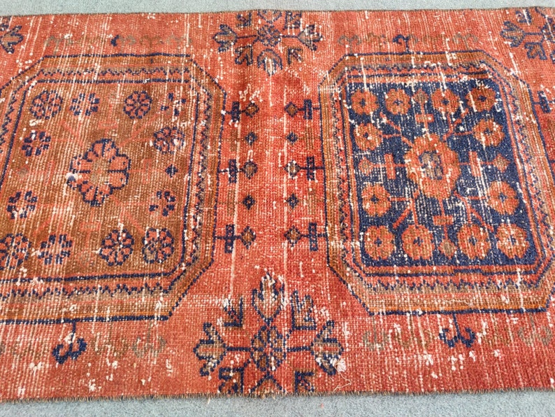 K&ouml;nnte beinhalten: Ein Vintage-Teppich mit einem verblassten roten Hintergrund und komplizierten blauen und orangefarbenen Blumenmustern. Der Teppich hat einen abgenutzten Look und ist mit einem traditionellen Design gewebt.