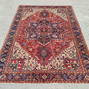 May include: A traditional Persian rug with a red, cream, and blue color scheme. The rug features a central medallion with intricate floral and geometric patterns. The rug has a dark blue border with a repeating pattern.