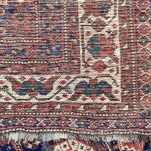 May include: Close-up of a red, blue and white patterned rug with a fringed edge. The rug has a traditional design with intricate details.