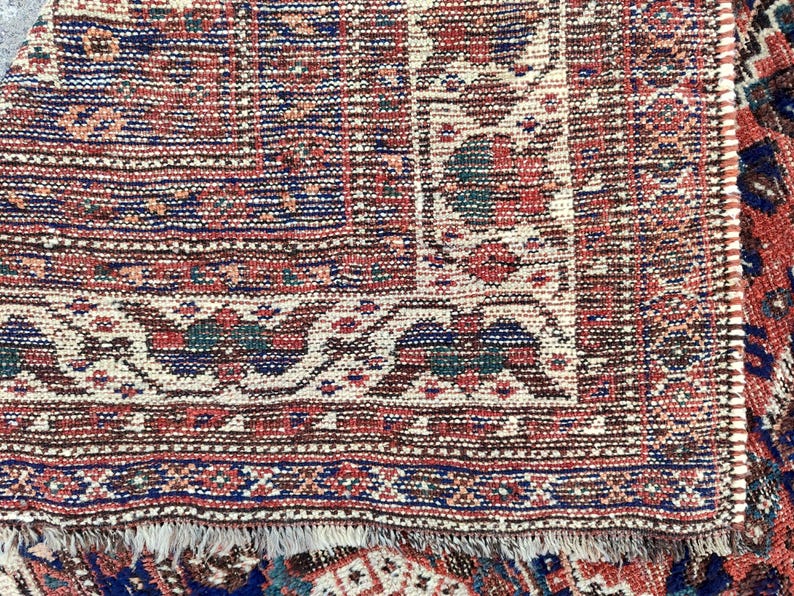 May include: Close-up of a red, blue and white patterned rug with a fringed edge. The rug has a traditional design with intricate details.