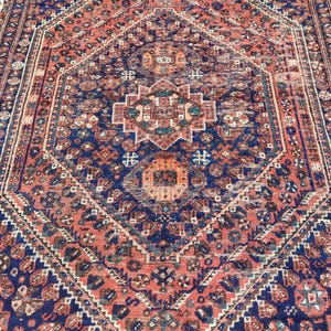 May include: A vintage Persian rug featuring a central diamond-shaped medallion in shades of blue, red, and cream. The rug has a detailed geometric pattern and a faded, worn appearance.