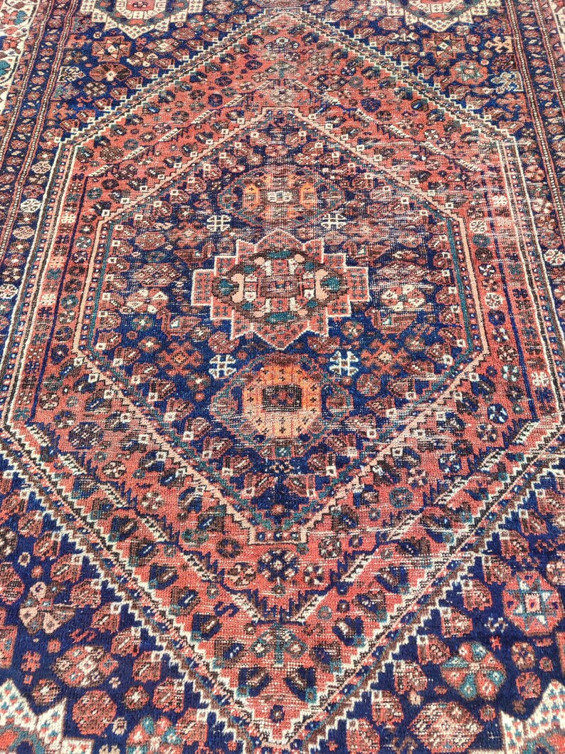 May include: A vintage Persian rug featuring a central diamond-shaped medallion in shades of blue, red, and cream. The rug has a detailed geometric pattern and a faded, worn appearance.