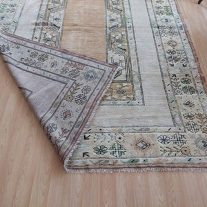 Puede incluir: Una alfombra beige con un patr&oacute;n geom&eacute;trico en tonos de marr&oacute;n, verde y crema. La alfombra tiene un borde de flecos y est&aacute; doblada por la mitad.