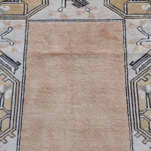 Puede incluir: Una alfombra beige con un patr&oacute;n geom&eacute;trico en tonos marrones, blancos y grises. La alfombra tiene un campo central y un borde con un dise&ntilde;o repetitivo.