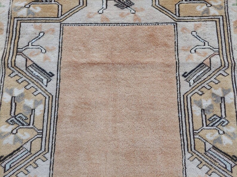 Puede incluir: Una alfombra beige con un patr&oacute;n geom&eacute;trico en tonos marrones, blancos y grises. La alfombra tiene un campo central y un borde con un dise&ntilde;o repetitivo.