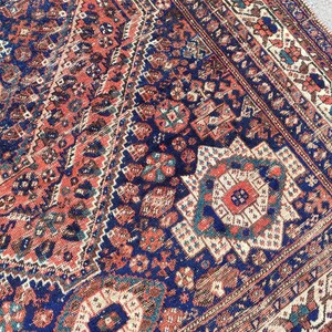 May include: A vintage Persian rug with an intricate geometric pattern in shades of red, blue, and white. The rug has a faded, worn look, giving it a unique character.