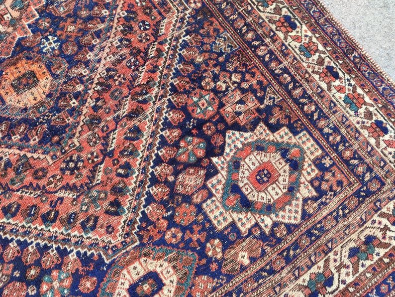 May include: A vintage Persian rug with an intricate geometric pattern in shades of red, blue, and white. The rug has a faded, worn look, giving it a unique character.