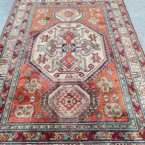 May include: A traditional rug with a red, beige, and blue geometric pattern. The rug has a central medallion with a repeating pattern of stylized flowers and leaves.