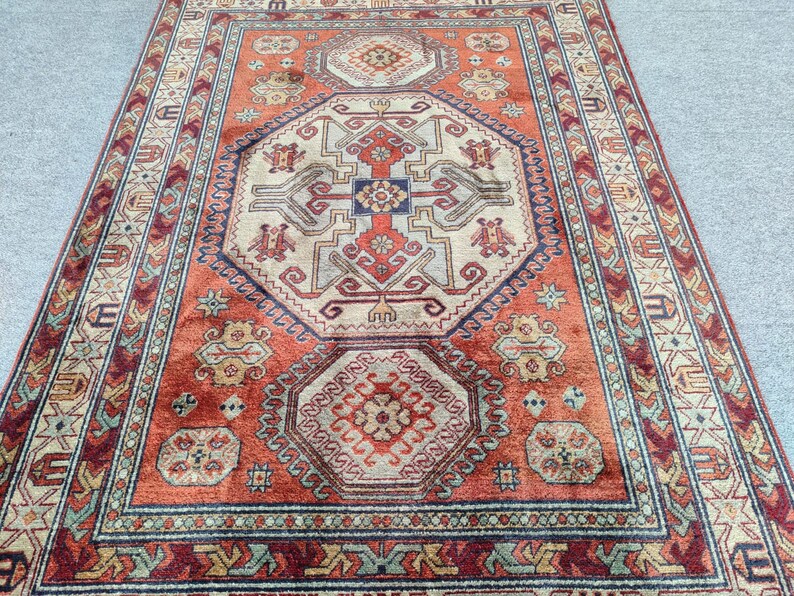 May include: A traditional rug with a red, beige, and blue geometric pattern. The rug has a central medallion with a repeating pattern of stylized flowers and leaves.