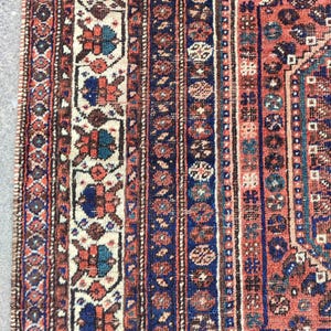 May include: Close-up of a red, blue and white patterned rug with intricate details. The rug has a traditional design with a central medallion and a border.