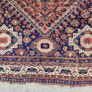 May include: A vintage Persian rug with a navy blue background and intricate patterns in shades of red, white, and cream. The rug has a fringed edge and a geometric design.
