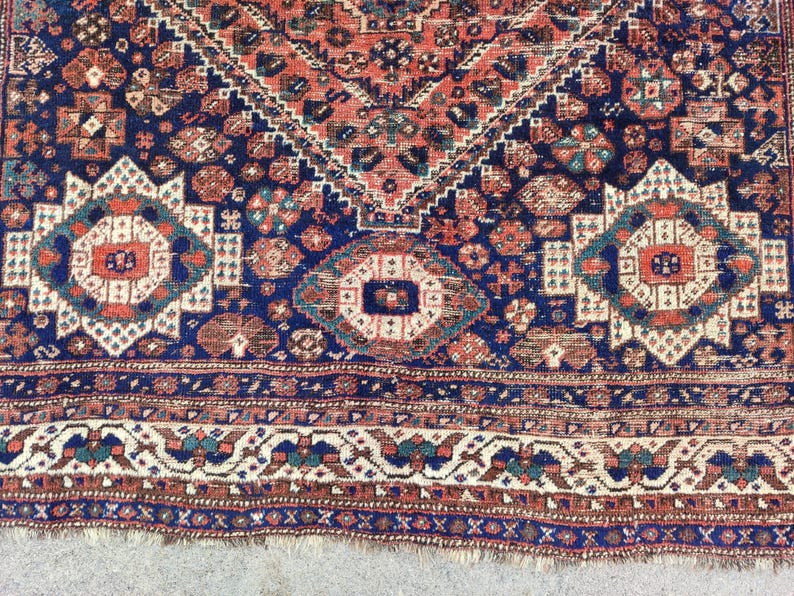 May include: A vintage Persian rug with a navy blue background and intricate patterns in shades of red, white, and cream. The rug has a fringed edge and a geometric design.