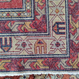 May include: Close-up of the edge of a red, beige, and blue patterned rug with a fringe border.