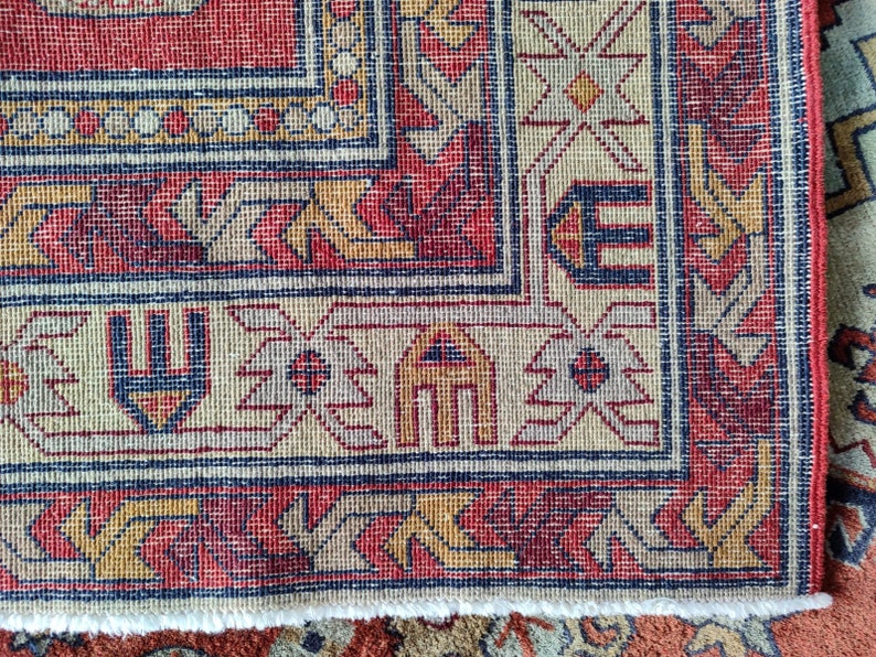 May include: Close-up of the edge of a red, beige, and blue patterned rug with a fringe border.