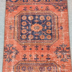 K&ouml;nnte beinhalten: Ein Vintage-Teppich mit rotem Hintergrund und einem marineblauen geometrischen Muster. Der Teppich hat einen verblassten, abgenutzten Look und ist aus Wolle.