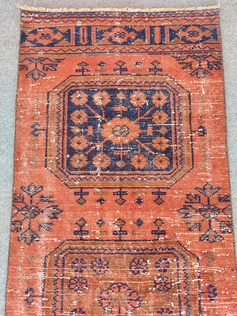 K&ouml;nnte beinhalten: Ein Vintage-Teppich mit rotem Hintergrund und einem marineblauen geometrischen Muster. Der Teppich hat einen verblassten, abgenutzten Look und ist aus Wolle.