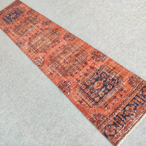 K&ouml;nnte beinhalten: Ein Vintage-L&auml;ufer mit rotem Hintergrund und aufwendigen blauen und orangefarbenen Blumenmustern. Der L&auml;ufer hat einen Fransenrand.