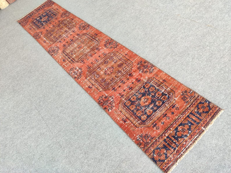 K&ouml;nnte beinhalten: Ein Vintage-L&auml;ufer mit rotem Hintergrund und aufwendigen blauen und orangefarbenen Blumenmustern. Der L&auml;ufer hat einen Fransenrand.