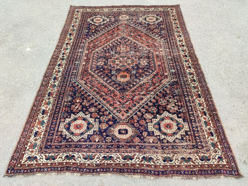May include: A vintage Persian rug with a navy blue background and intricate red, white, and cream patterns. The rug has a diamond-shaped centre with a floral design and a border with a repeating geometric pattern.