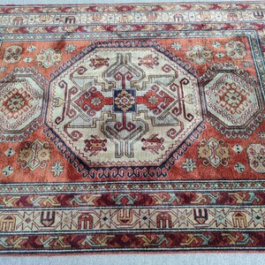 May include: A traditional rug with a red, beige, and blue color scheme. The rug features a central medallion with intricate geometric patterns and a border with repeating motifs.