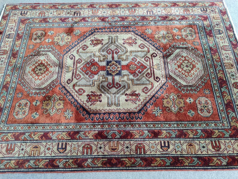 May include: A traditional rug with a red, beige, and blue color scheme. The rug features a central medallion with intricate geometric patterns and a border with repeating motifs.