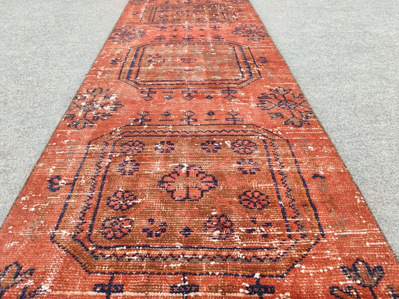 K&ouml;nnte beinhalten: Ein vintage roter und blauer L&auml;uferteppich mit geometrischem Muster. Der Teppich hat einen abgenutzten Look und ist aus Wolle.