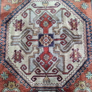 May include: A traditional rug with a geometric pattern in shades of red, blue, beige, and brown. The rug features a central medallion with intricate details and a repeating border.