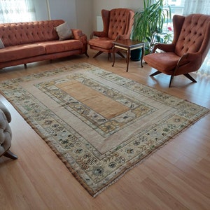 Puede incluir: Una alfombra beige y marr&oacute;n con estampado y un centro marr&oacute;n claro, colocada sobre un suelo de madera dura en un sal&oacute;n. Dos sillones marrones y un sof&aacute; marr&oacute;n est&aacute;n dispuestos alrededor de la alfombra.