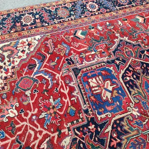 May include: A detailed Persian rug with a red background and intricate floral and geometric patterns in shades of blue, white, and beige. The rug has a border with a dark blue background and a gold trim.