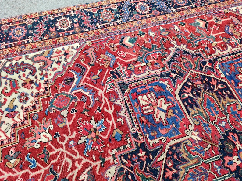 May include: A detailed Persian rug with a red background and intricate floral and geometric patterns in shades of blue, white, and beige. The rug has a border with a dark blue background and a gold trim.