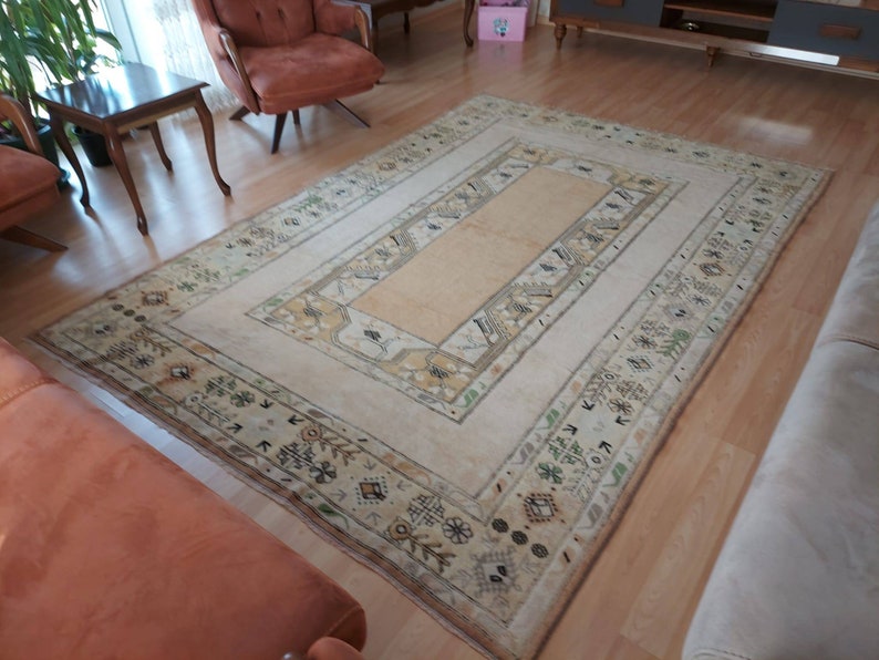 Puede incluir: Una alfombra de color crema con un centro beige y un borde estampado. La alfombra tiene un dise&ntilde;o geom&eacute;trico con peque&ntilde;os motivos repetidos en tonos marrones, verdes y beige.