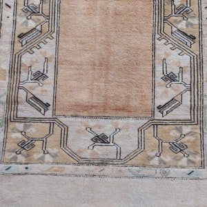 Puede incluir: Una alfombra beige con un borde de patr&oacute;n geom&eacute;trico marr&oacute;n y negro. La alfombra tiene un centro marr&oacute;n claro.