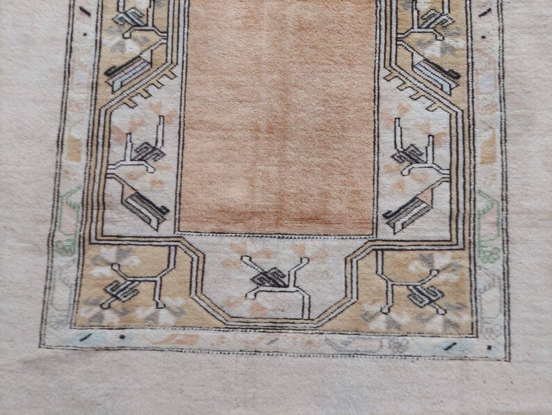 Puede incluir: Una alfombra beige con un borde de patr&oacute;n geom&eacute;trico marr&oacute;n y negro. La alfombra tiene un centro marr&oacute;n claro.