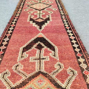 May include: A vintage Turkish runner rug with a red background and intricate geometric patterns in black, white, and cream. The rug has a fringed edge and is made of wool.