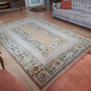 Puede incluir: Una alfombra vintage de color crema con un patr&oacute;n geom&eacute;trico en tonos marrones, beige y verdes. La alfombra tiene un panel rectangular central con un panel rectangular m&aacute;s peque&ntilde;o en su interior. La alfombra est&aacute; colocada sobre un suelo de madera.