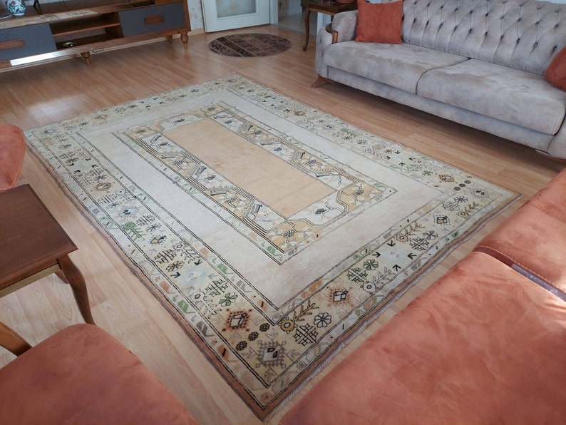 Puede incluir: Una alfombra vintage de color crema con un patr&oacute;n geom&eacute;trico en tonos marrones, beige y verdes. La alfombra tiene un panel rectangular central con un panel rectangular m&aacute;s peque&ntilde;o en su interior. La alfombra est&aacute; colocada sobre un suelo de madera.