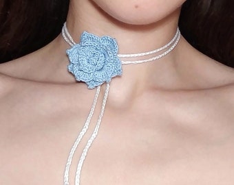 Può includere: Un girocollo in crochet bianco con un ciondolo a forma di fiore in crochet blu chiaro.