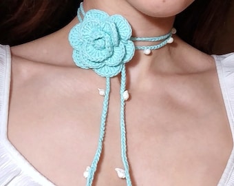 Può includere: Un girocollo di fiori all'uncinetto di colore azzurro chiaro con perline bianche. Il girocollo è lungo e ha un aspetto delicato e femminile.