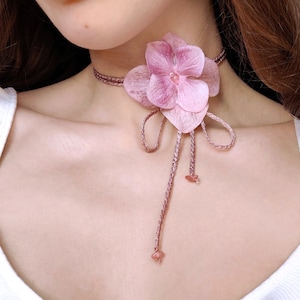 May include: A pink flower choker necklace with a delicate flower design and a long, thin cord with a pink bead at the end.