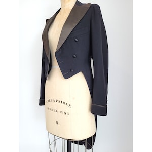 May include: A black tailcoat with a satin shawl collar and a single button closure. The tailcoat has a long, flowing tail and is made of a smooth, luxurious fabric.