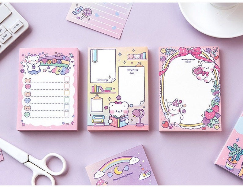 Puede incluir: Tres blocs de notas rosas con lindos ositos de dibujos animados y dise&ntilde;os de arco&iacute;ris. Los blocs de notas tienen diferentes t&iacute;tulos: "To Do", "Love Story" y "Morning Bear".