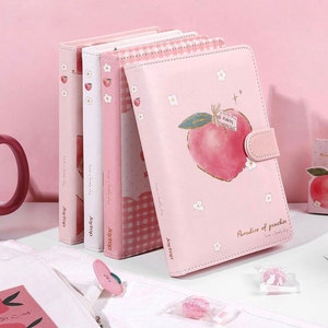May include: Four pink notebooks with peach designs and the text "Love a lovely day" and "Joytop". The front cover of the notebook on the right has a peach with a tag that says "beary" and the text "Paradise of peaches".