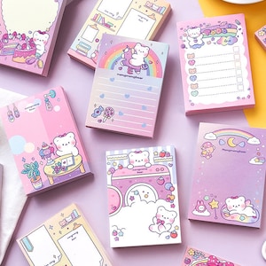 Puede incluir: Un conjunto de blocs de notas rosas y morados con lindas ilustraciones de osos y dise&ntilde;os de arco&iacute;ris. Los blocs de notas presentan diferentes dise&ntilde;os, incluyendo un oso montando un unicornio, un oso leyendo un libro y un oso con un pastel. Los blocs de notas son perfectos para tomar notas, escribir listas o dejar mensajes.