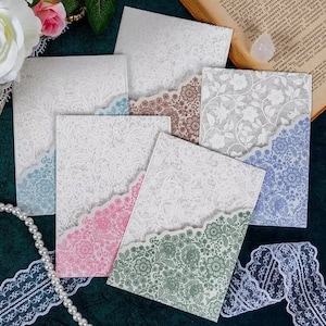 May include: Six white envelopes with different floral patterns on the front. The envelopes are arranged in a semi-circle on a green surface.