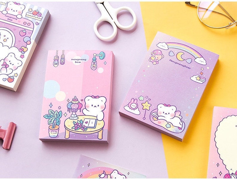 Puede incluir: Un conjunto de blocs de notas adhesivas de color rosa pastel y morado con osos de dibujos animados adorables con el texto "Hongmeimeibear". Las notas est&aacute;n decoradas con estrellas, nubes y arco&iacute;ris.